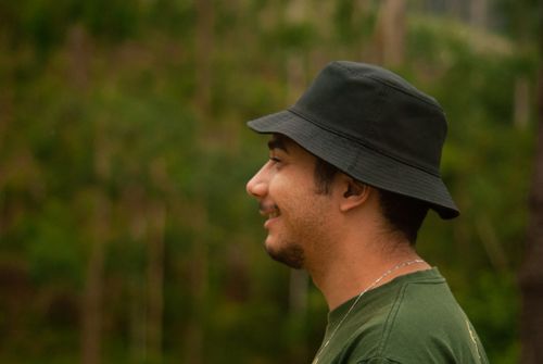 Free A smiling man wearing a green shirt and black hat outdoors. Lush greenery in the background. Stock Photo
