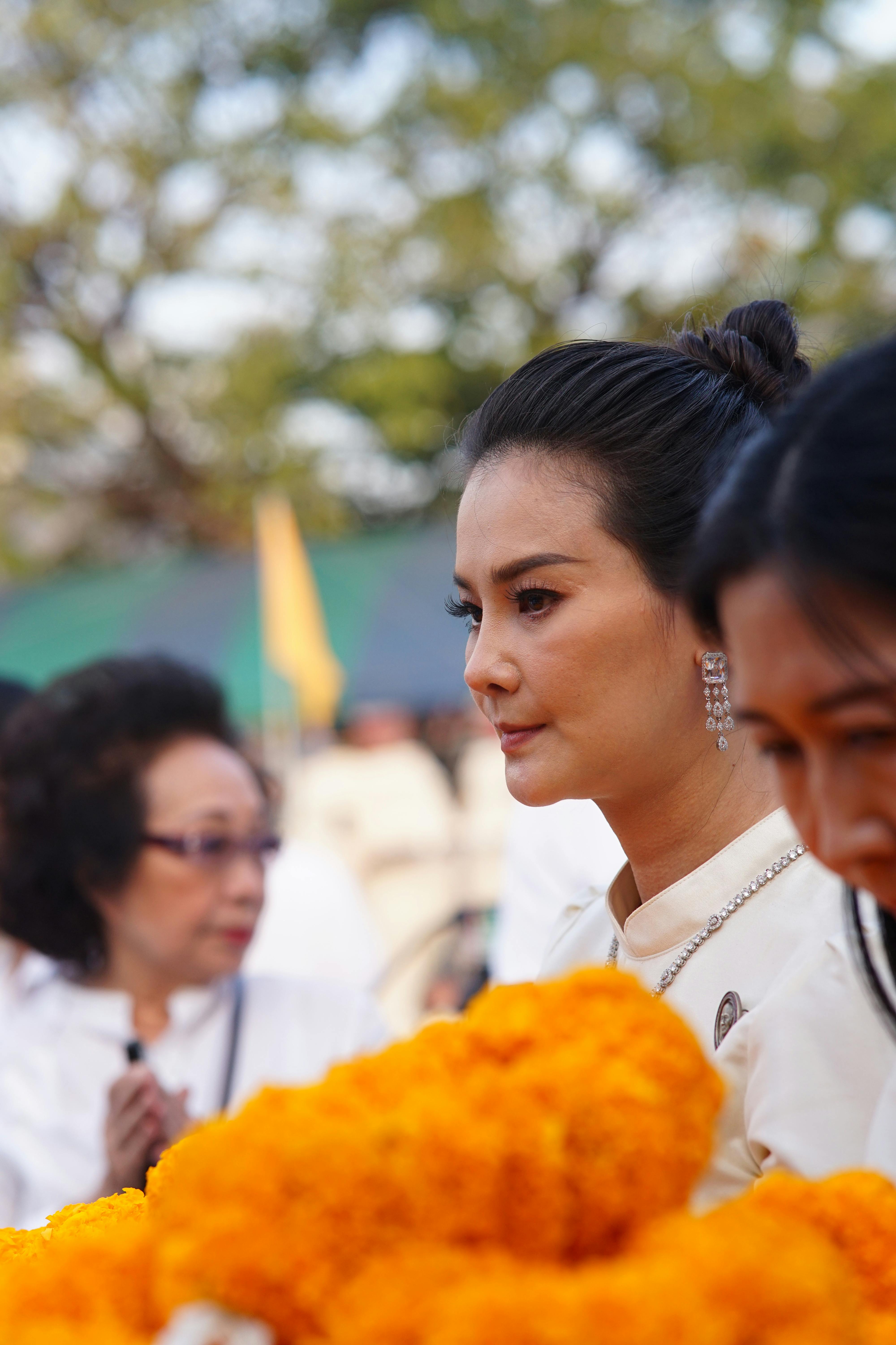 Portrait of an elegant woman at an outdoor social event with vibrant orange flowers in focus.