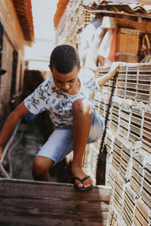 Free A child in casual clothes climbs a wooden fence between two buildings outdoors. Stock Photo