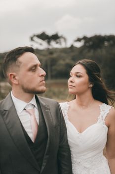 A newlywed couple poses elegantly outdoors in wedding attire, captured in a serene countryside.