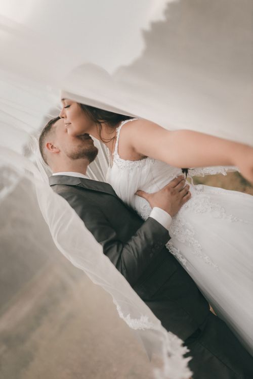 Free A touching moment capturing a newlywed couple embracing under a flowing veil outdoors. Stock Photo