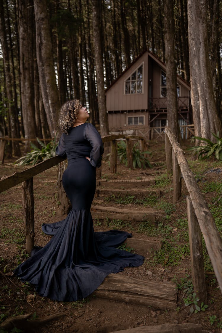 Woman In A Long Dress Standing On Steps In Front Of A House In Woods 