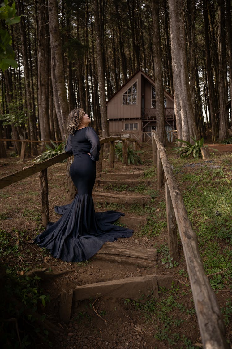 Woman In A Long Dress Standing On Steps In Front Of A House In Woods 