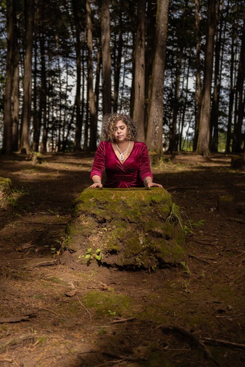 Pretty Woman in Red Dress Posing by Rock in Forest
