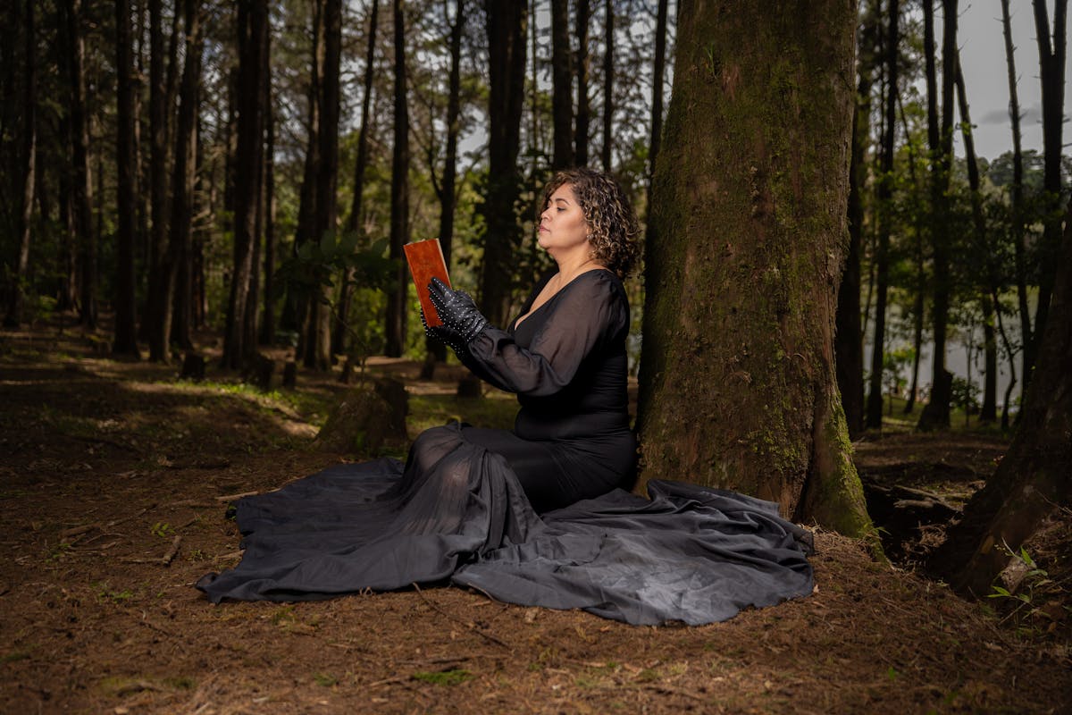 Persona seduta sotto un grande albero mentre legge un libro nella foresta