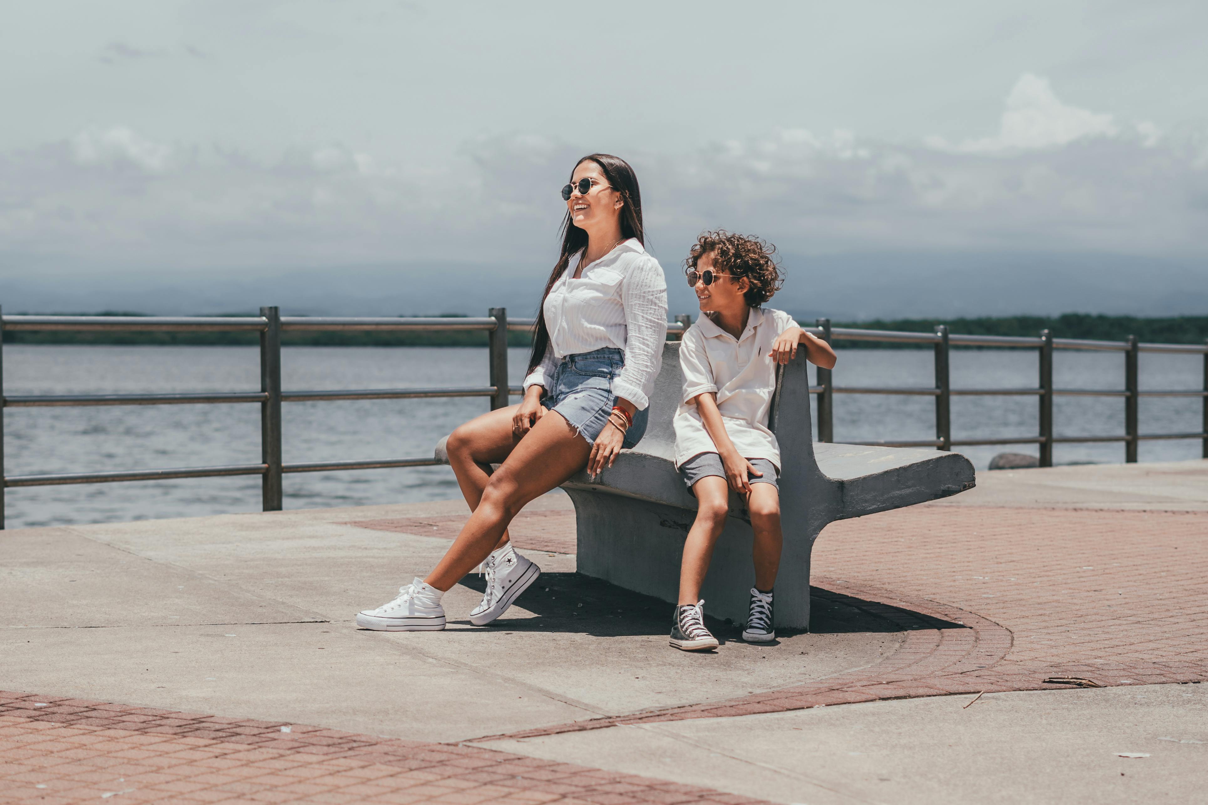 A woman and a boy sitting on a bench near the water