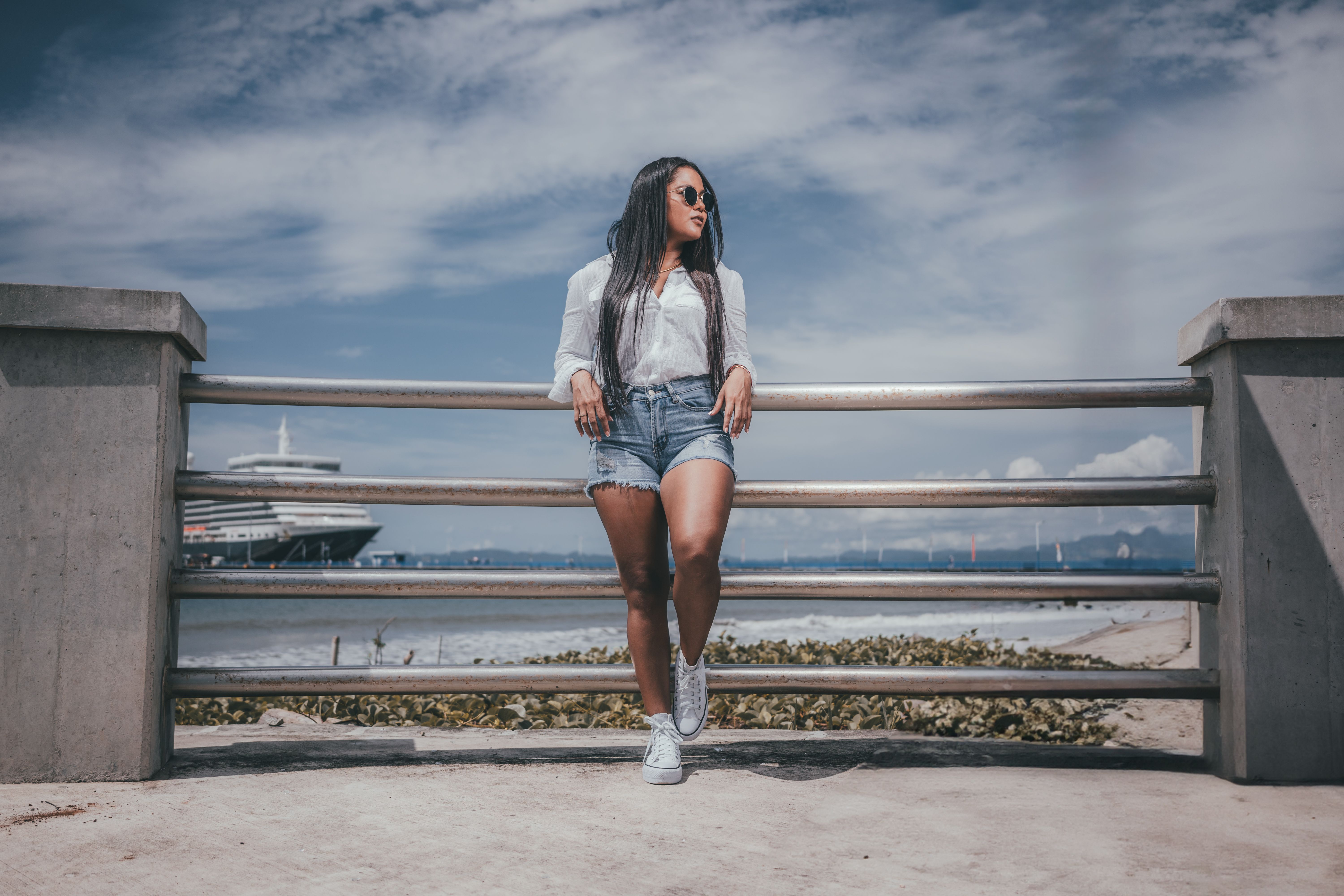 A stylish woman in shorts and sunglasses relaxes by the coast, enjoying a sunny day.