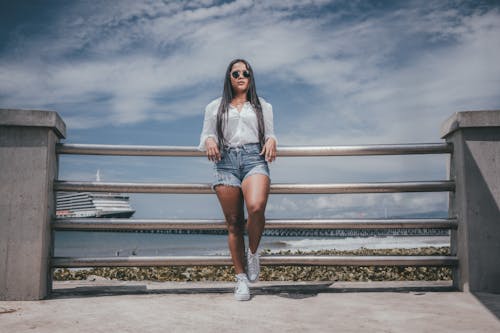 Woman in Shorts and Sunglasses Standing on a Pier on the Background of Sea and Ship 