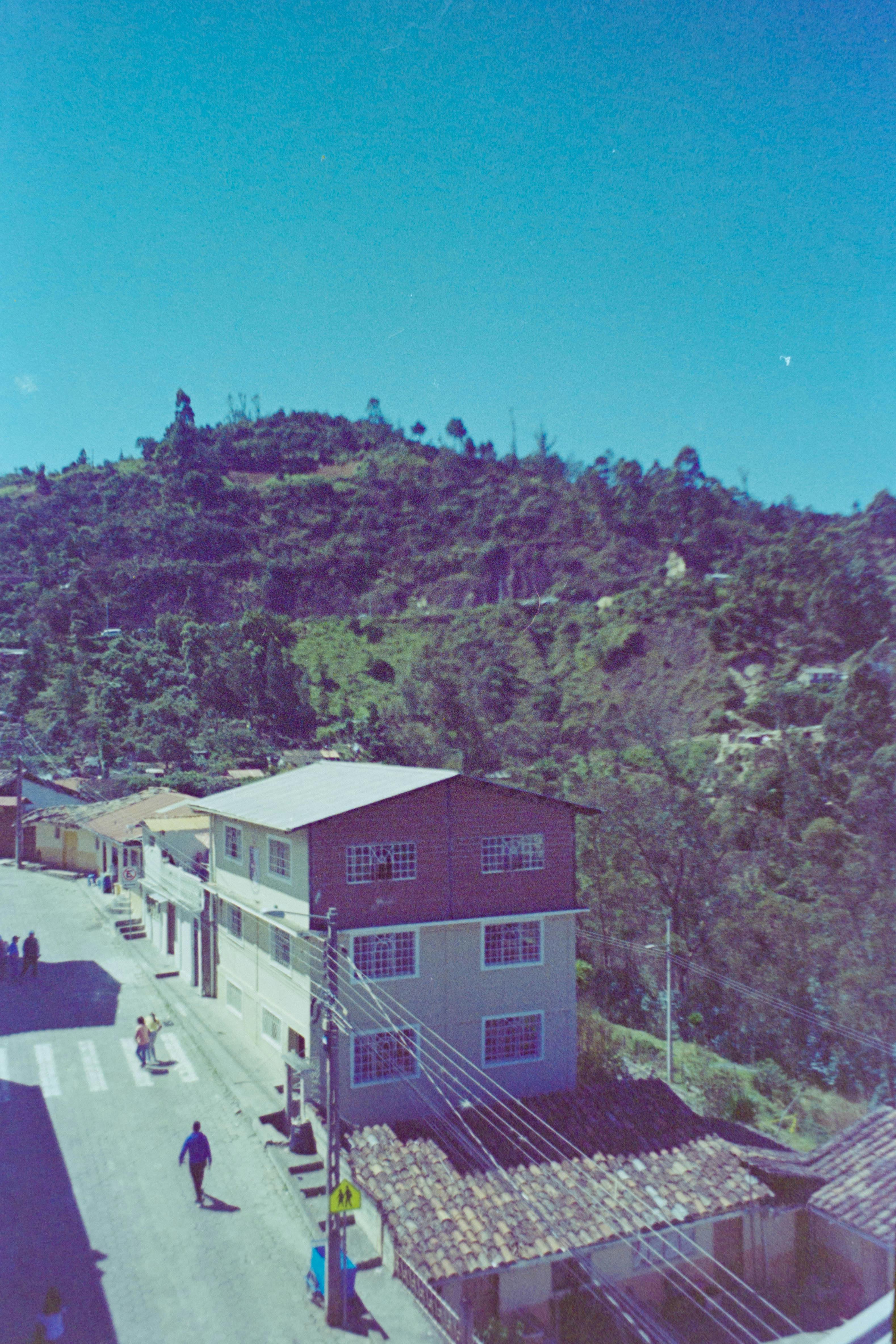 A scenic view of a village with houses and lush green mountains under a clear blue sky.