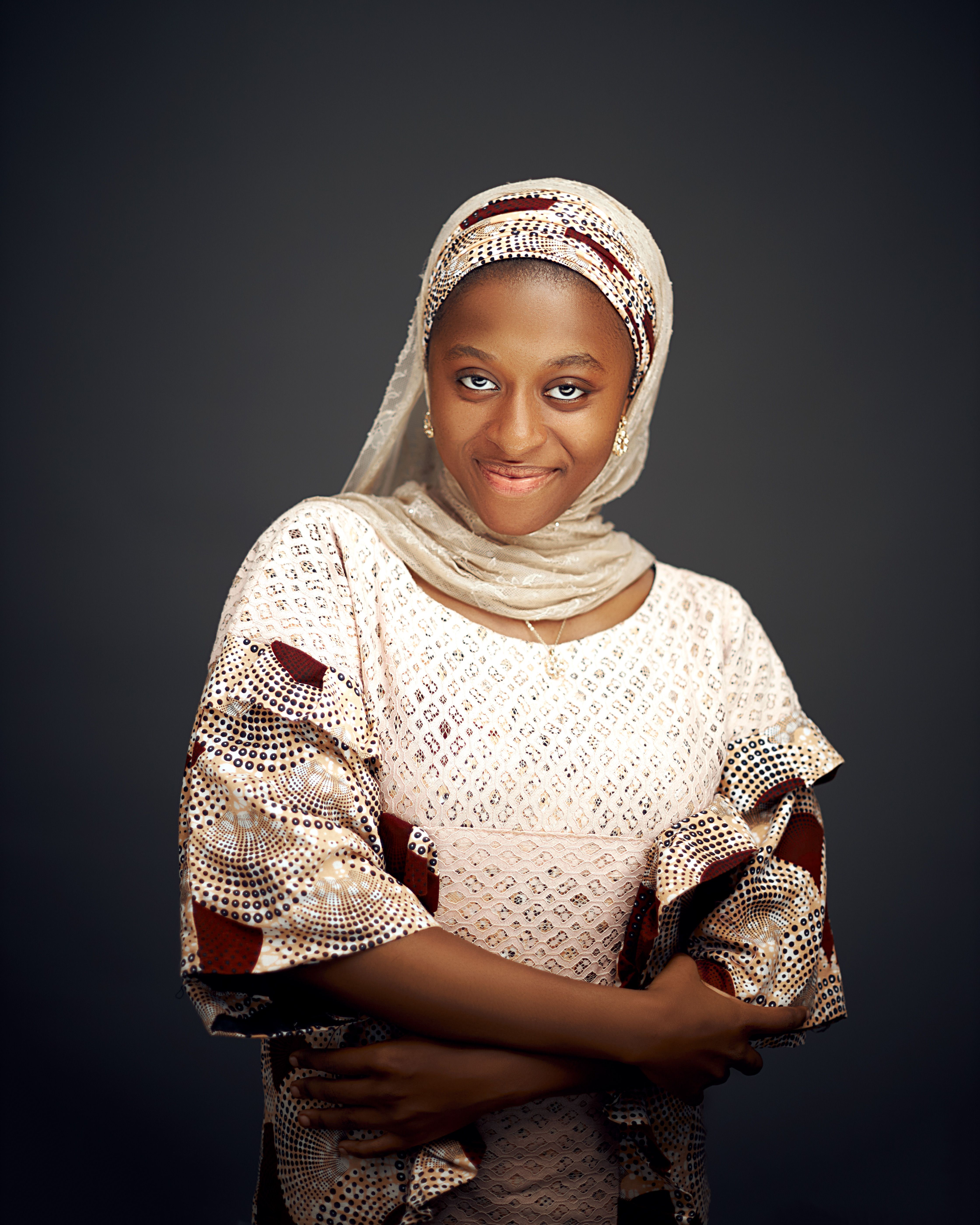 Smiling woman in traditional clothing with a headscarf on a gray background.