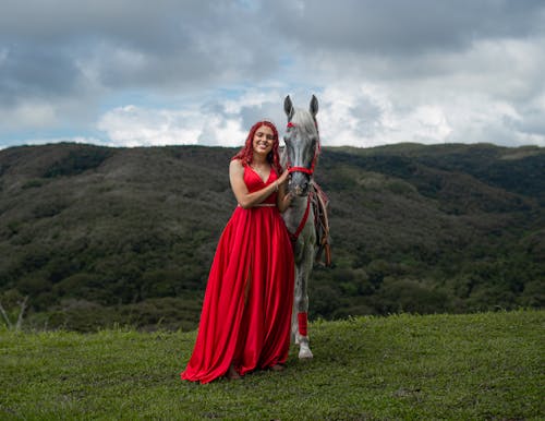 Portrait of a Young Woman Wearing a Red Evening Gown Posing Outdoors with a Horse