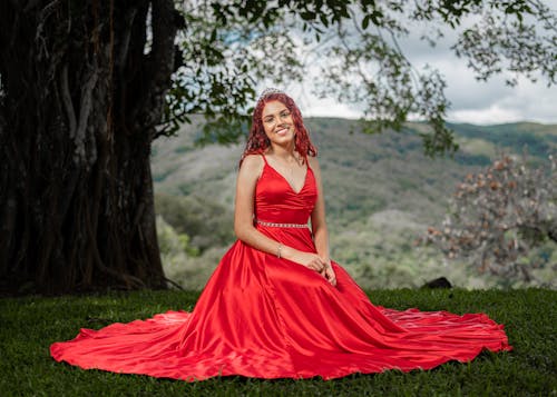 Portrait of a Female Model Wearing a Red Dress Sitting on the Grass