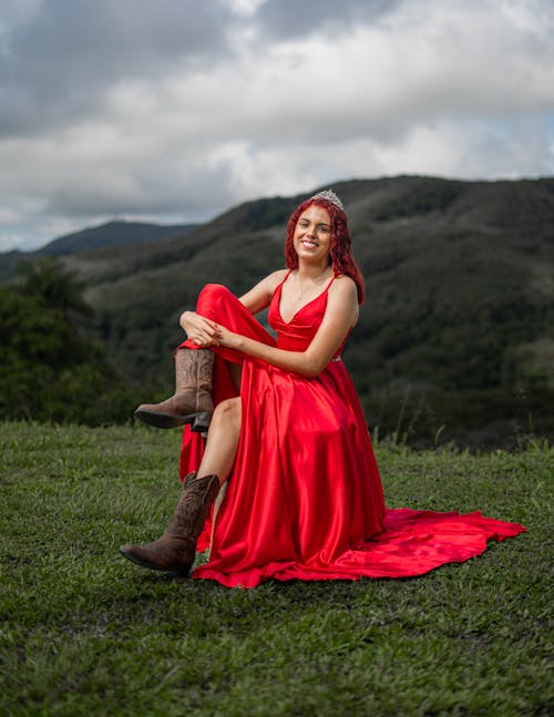 Portrait of a Female Model Wearing a Red Dress Sitting on a Grassy Hill