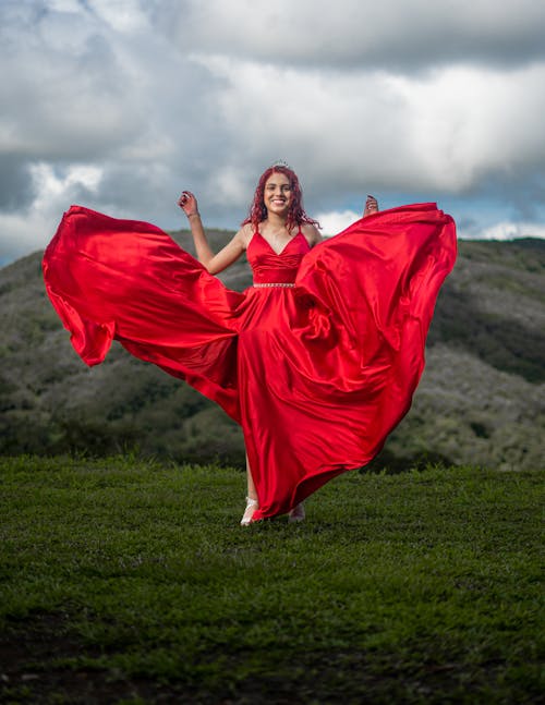 Portrait of a Female Model Wearing a Red Dress Standing on a Grassy Hill
