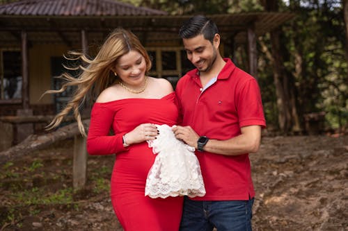 Pregnant Couple Standing Outdoors with a Baby Dress in Hands