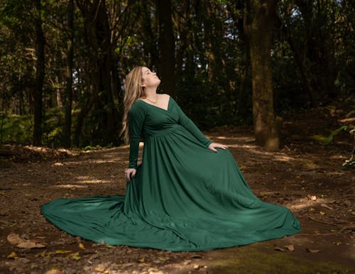 Pregnant Woman in a Green Dress Sitting in a Forest 