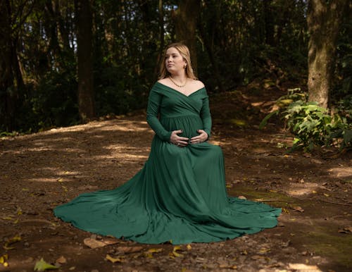 Pregnant Woman Wearing a Green Elegant Dress Sitting in a Forest