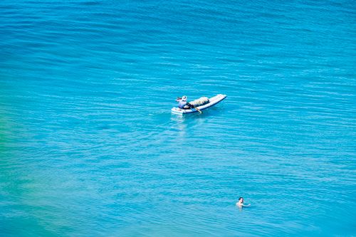 Free A person rowing a small boat in the middle of a clear, blue sea with a swimmer nearby. Stock Photo