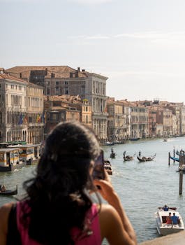 A woman photographs a bustling Venetian canal with gondolas and historic architecture.