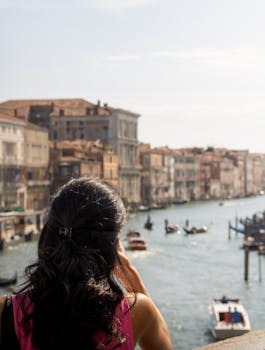 Experience Venice from a unique angle with a woman enjoying the view of the Grand Canal's vibrant life.