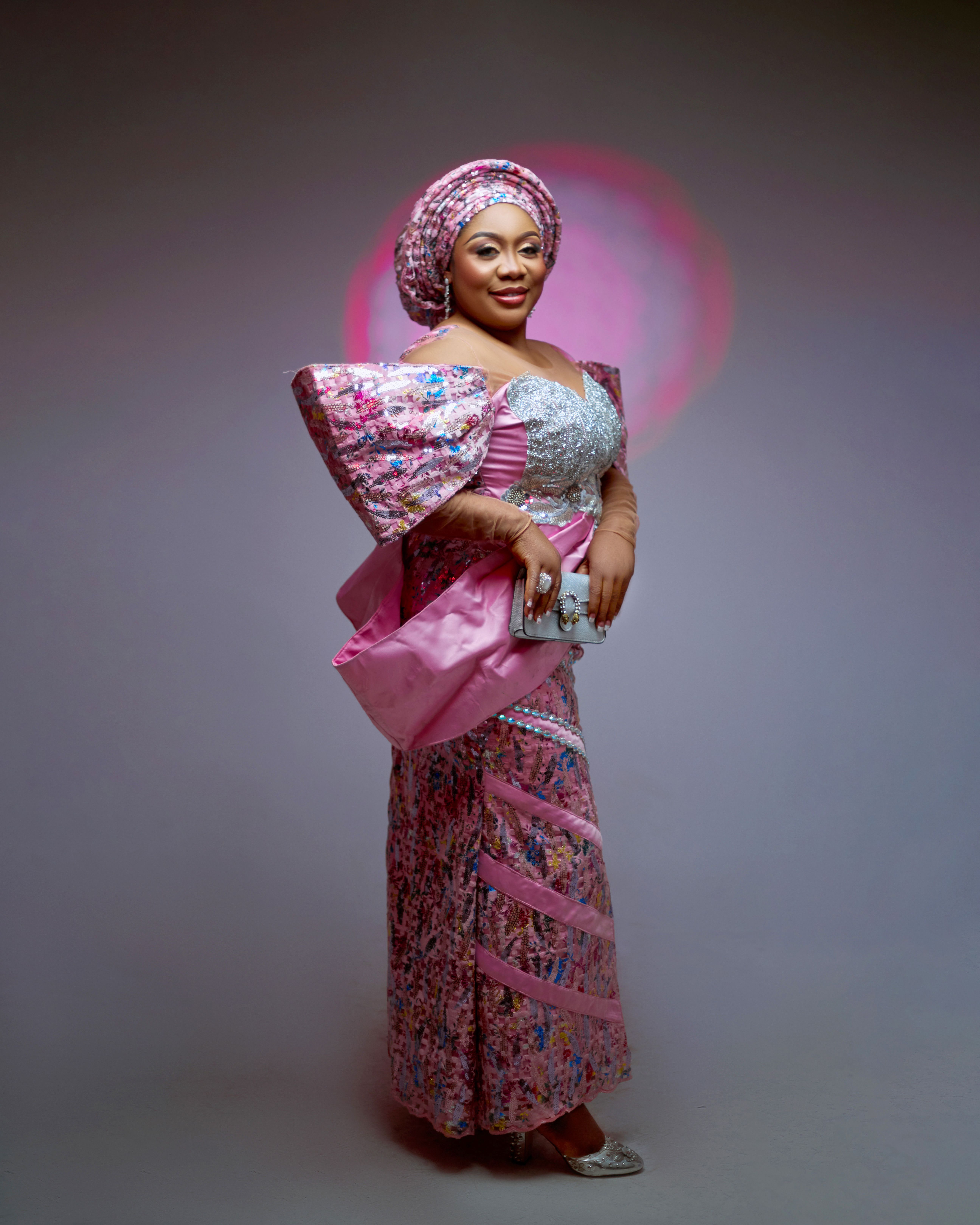 Sophisticated portrait of a woman dressed in pink traditional clothing, adorned with a headpiece, captured in a studio setting.