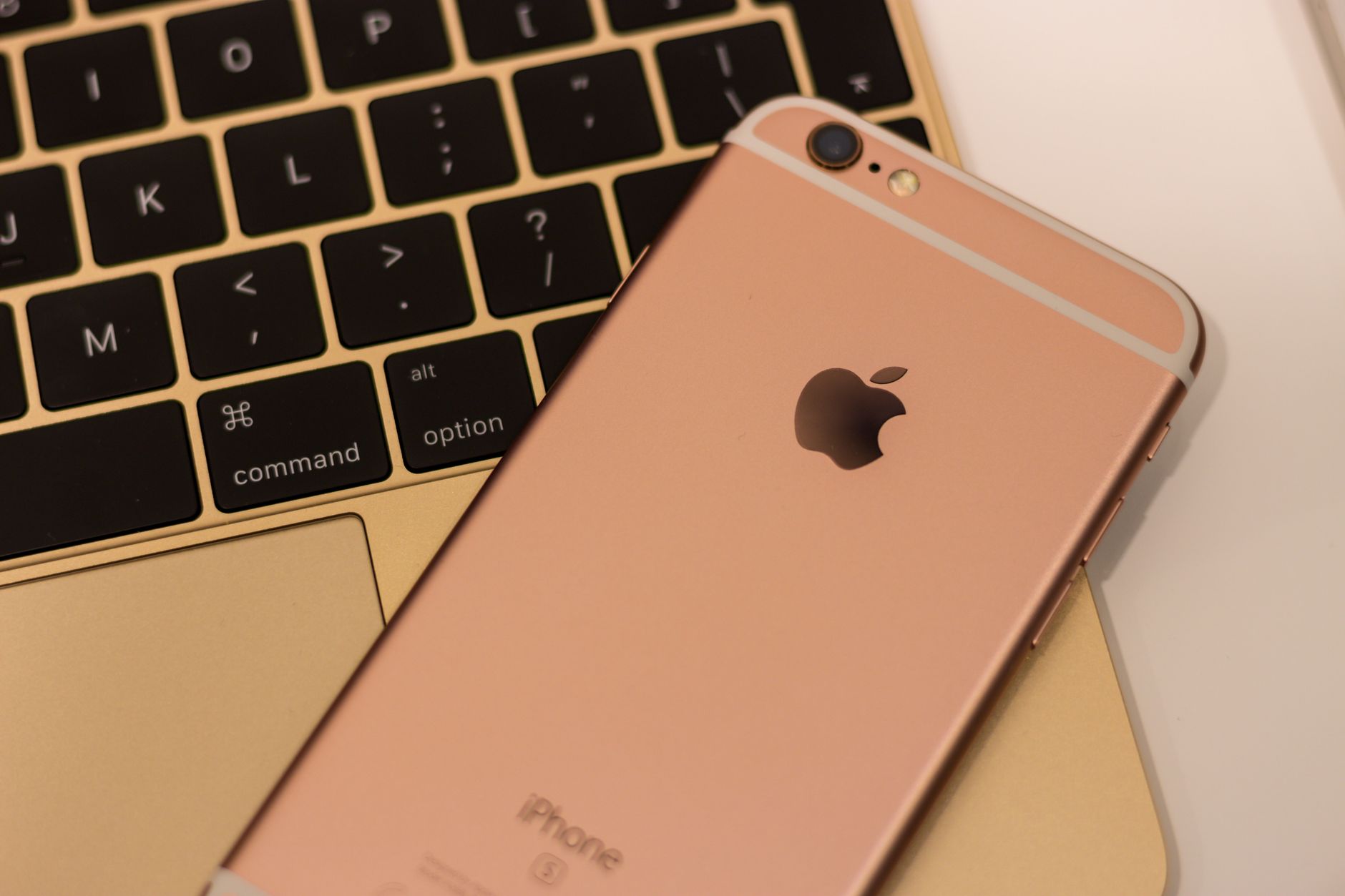 Close-up of a rose gold iPhone 6s placed on a MacBook keyboard, showcasing sleek design and modern technology.