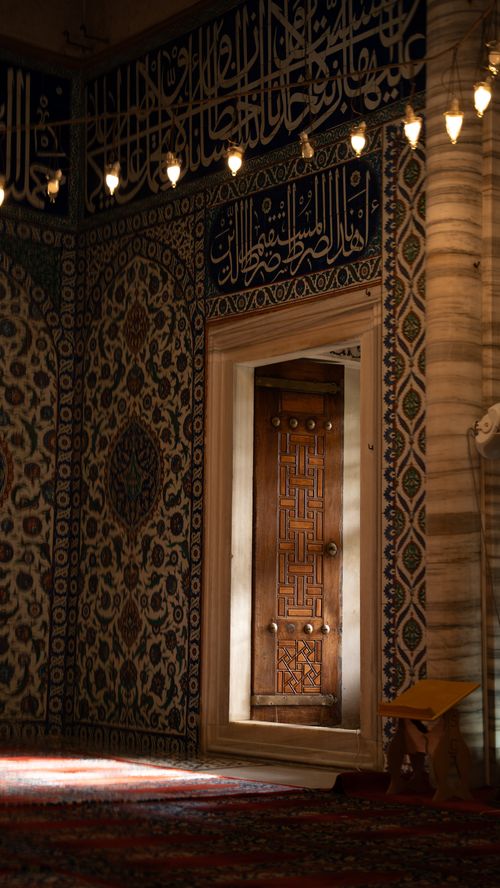 Free Beautiful mosque interior showcasing detailed patterns and a wooden doorway bathed in soft light. Stock Photo