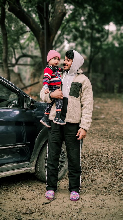 Free A father holding his daughter beside a car in an outdoor setting, both wearing winter clothing. Stock Photo