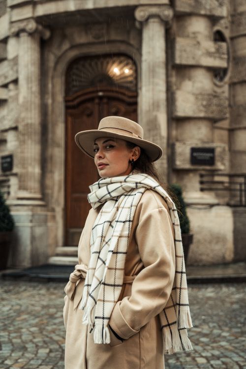 Free Elegant woman in a hat and scarf poses confidently on an urban cobblestone street. Stock Photo