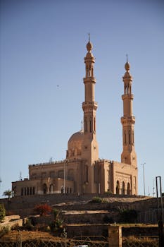 Beautiful view of a traditional mosque with towering minarets in Louxor, Egypt under a clear blue sky.