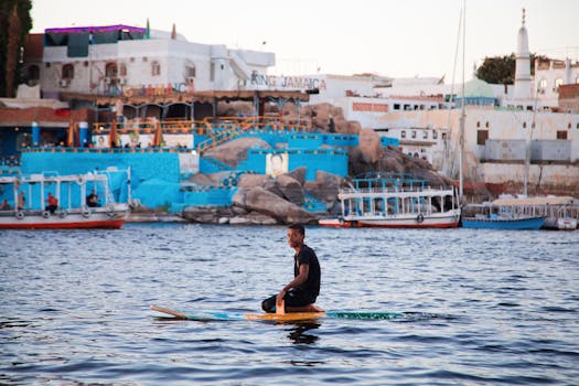 A young man enjoying paddleboarding in front of colorful riverside architecture on the Nile in Luxor, Egypt.