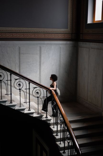 Woman in a black dress climbs a classic marble staircase in Istanbul.