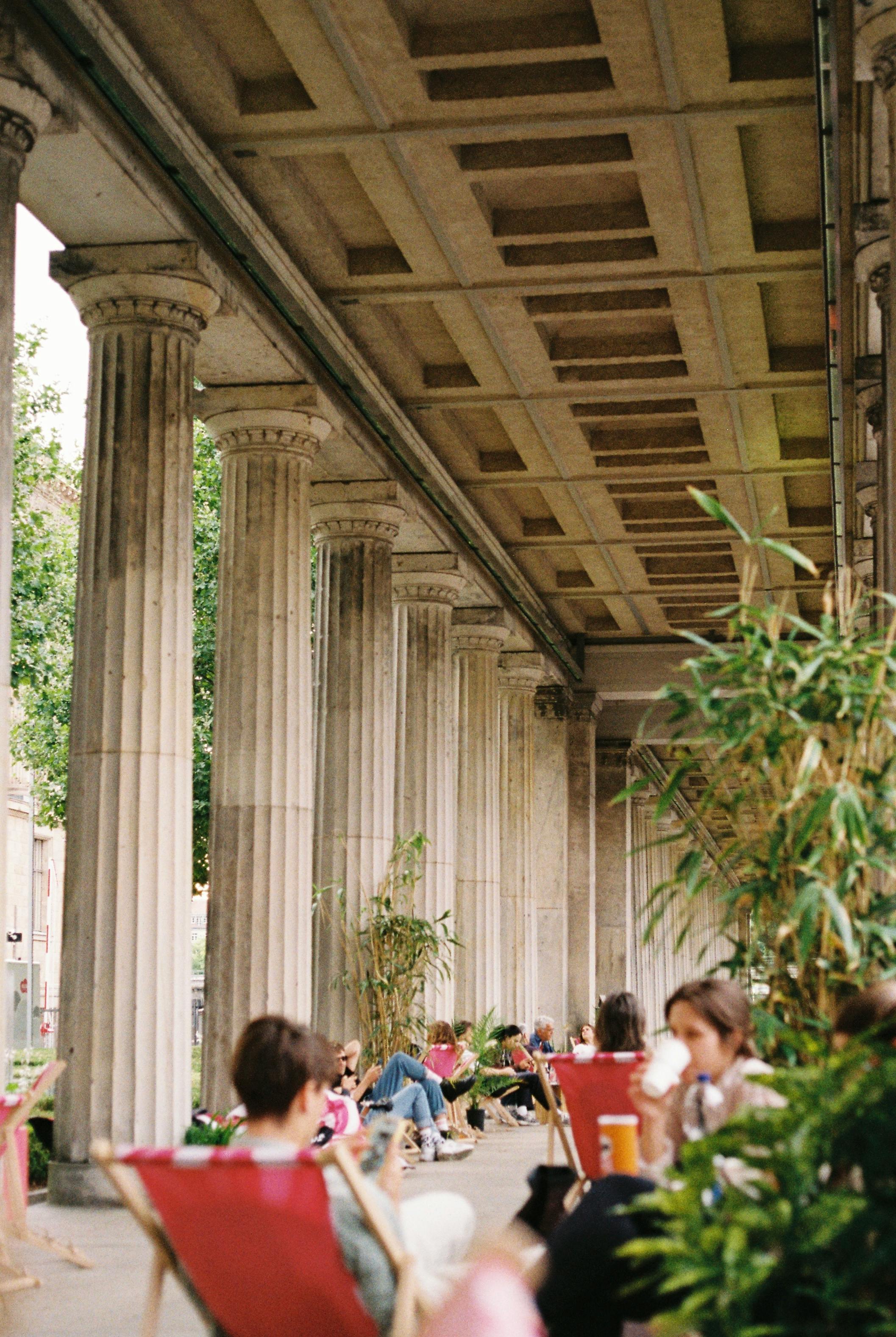 People relaxing in a café setting with historic columns in Berlin, Germany.