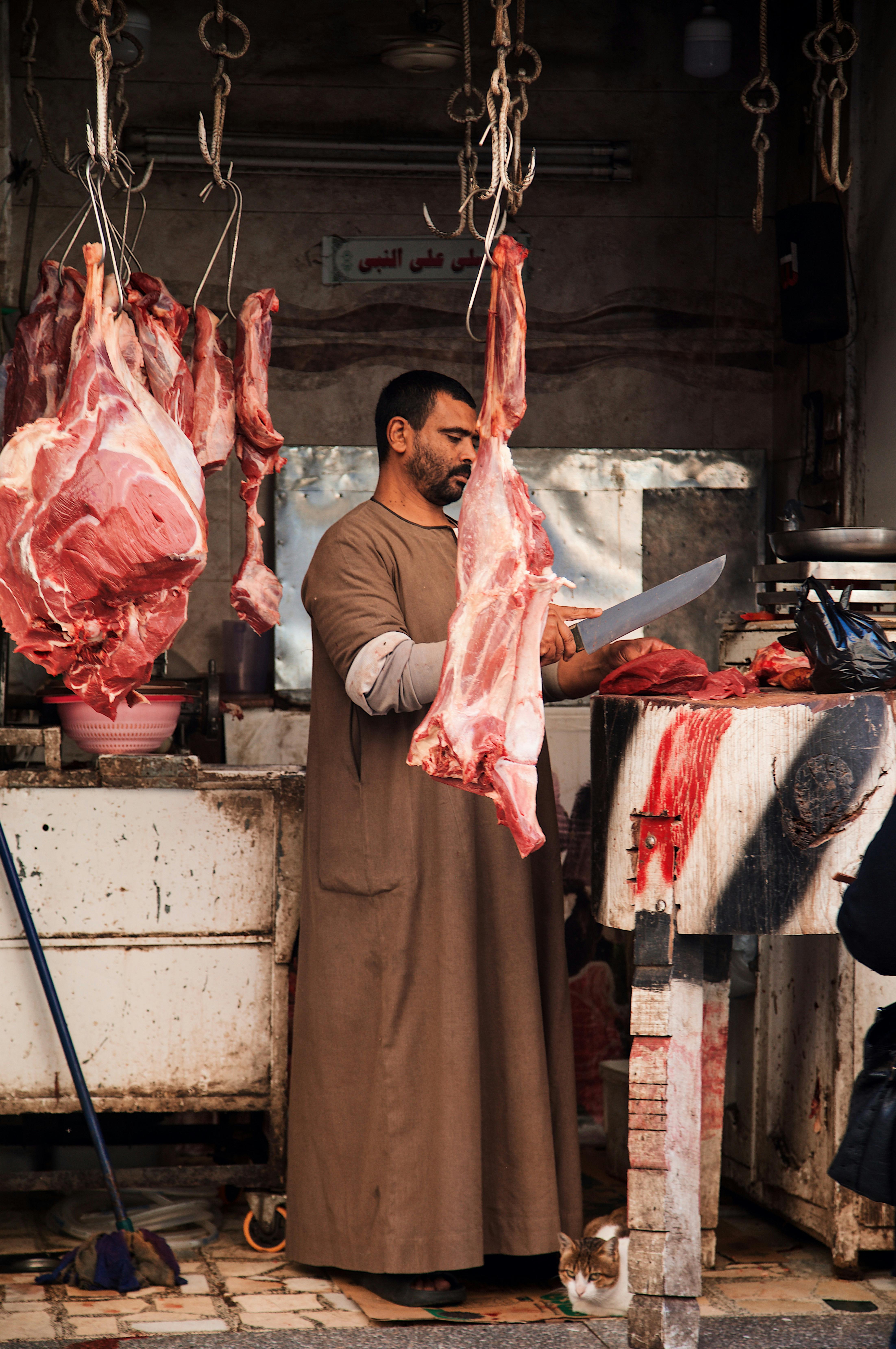 a man in a brown robe standing in front of a butcher shop