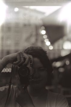 A woman capturing a self-portrait using an analog camera outdoors.
