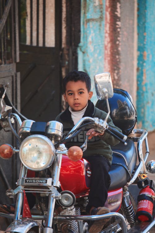 A young boy sitting on a motorcycle in front of a building
