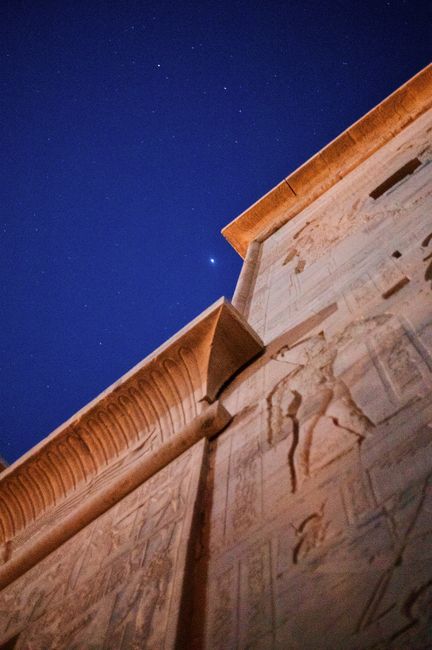 A detailed view of an ancient Egyptian temple wall under a starry sky at night.