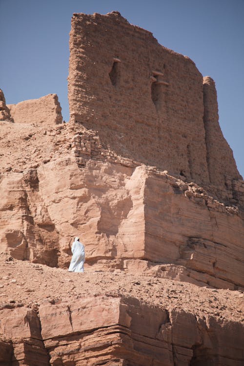 A man in white robes stands on top of a rock