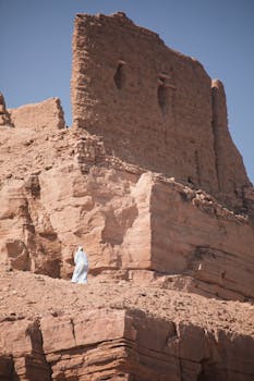 A solitary figure in traditional attire near ancient ruins in the Egyptian desert.
