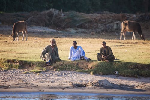 Three men sitting on the ground next to a river