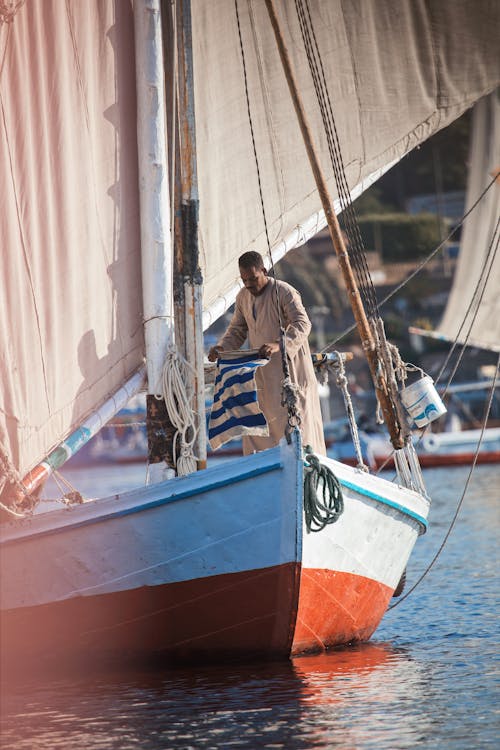 A man is standing on the deck of a sailboat