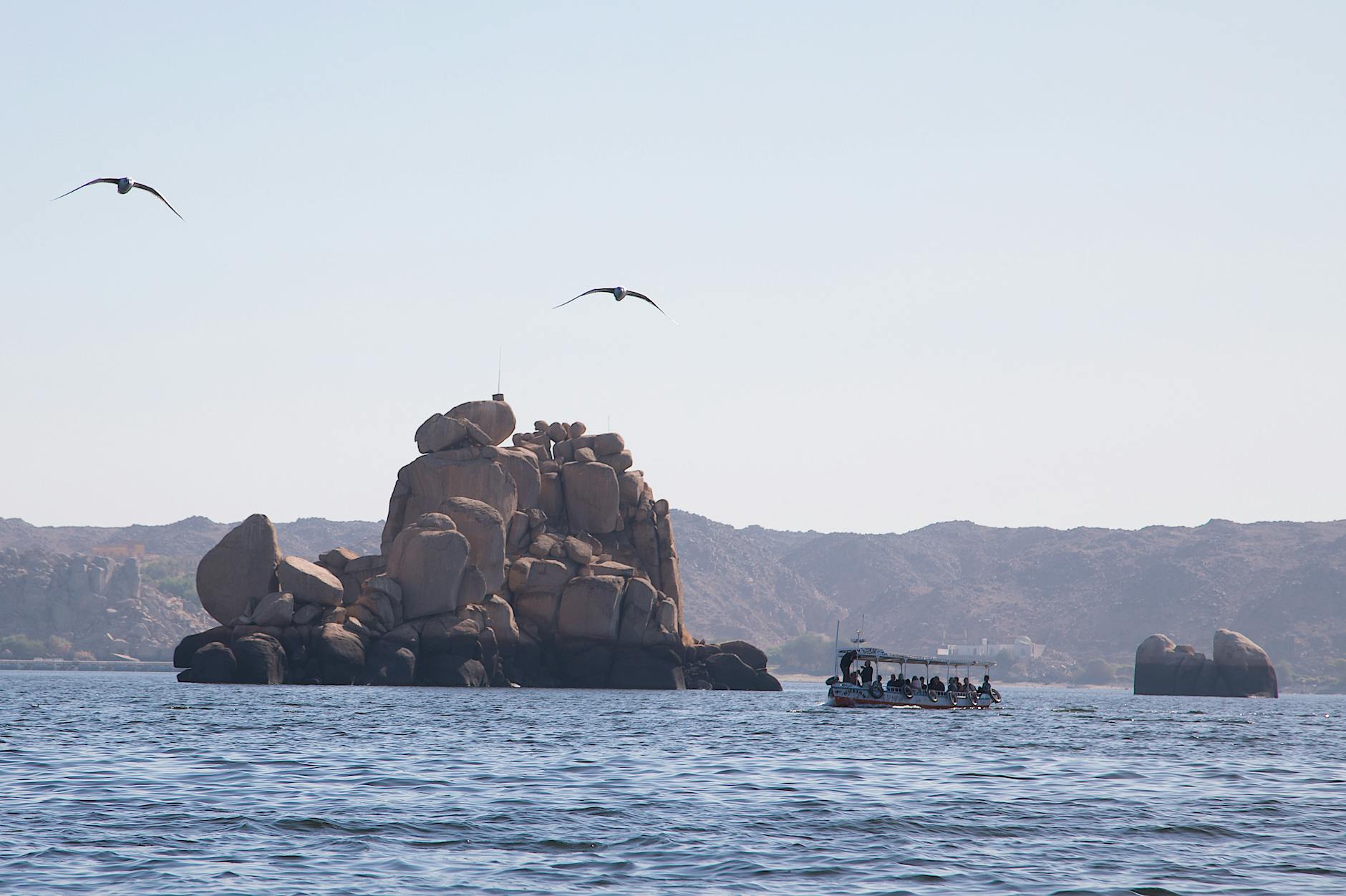 Tourists enjoy a tranquil boat ride on the Nile with a rocky island backdrop in Egypt.