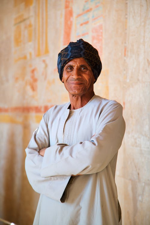 An old man in a turban standing in front of a wall