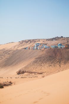 A serene desert scene with a distant camel caravan and vibrant oasis buildings, evoking adventure.