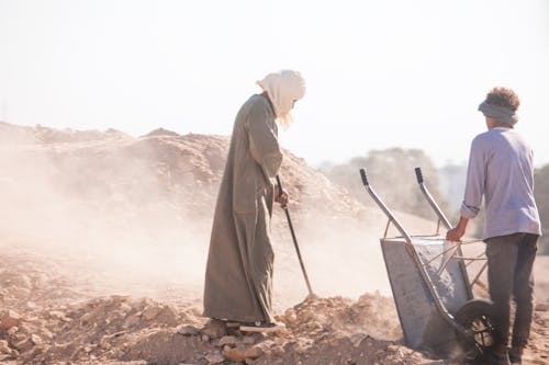 Two men are working in the sand with a wheelbarrow