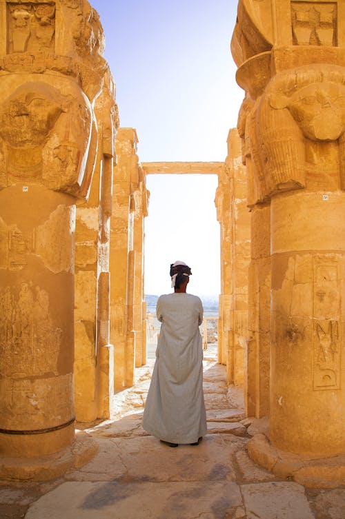 A woman in a white dress stands in front of a large stone building