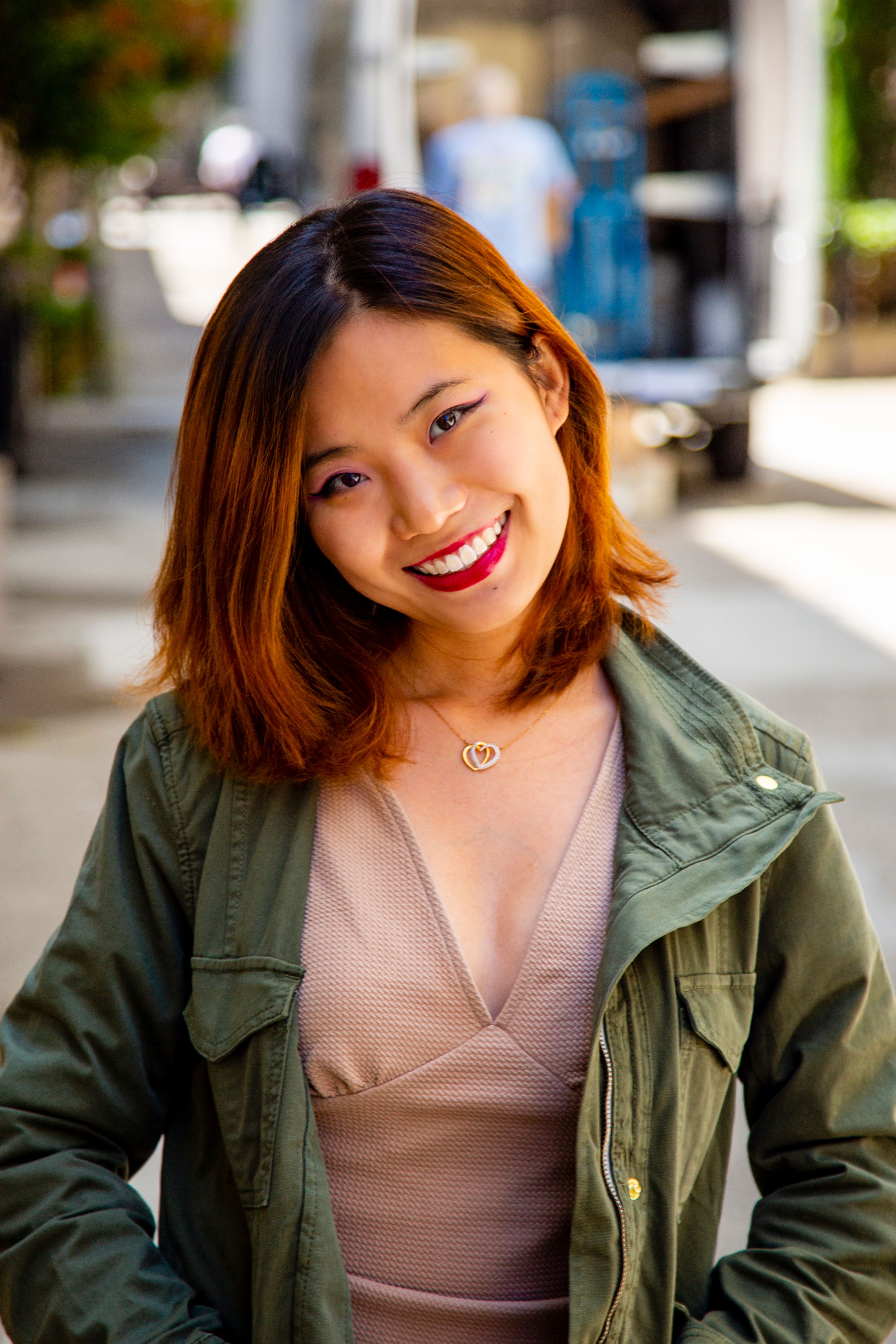 A cheerful young woman in a stylish green jacket poses on a sunny San Francisco street.
