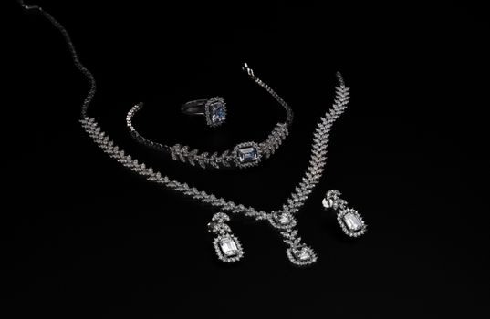 Elegant diamond jewelry set including necklace, bracelet, ring, and earrings on a black backdrop.