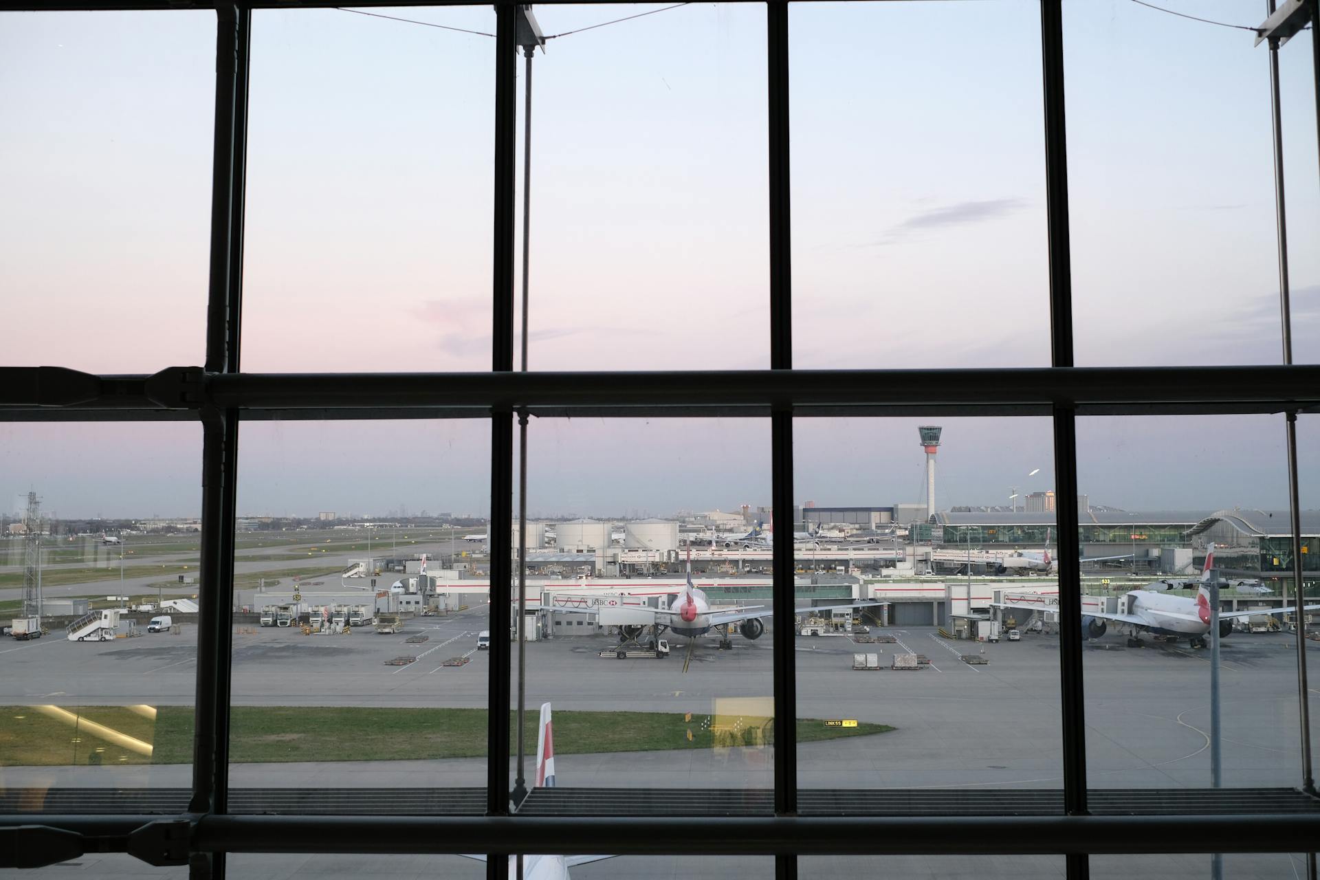 View of Heathrow Airport tarmac and airplanes through terminal window during twilight.