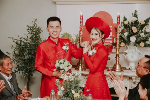 Elegant Vietnamese couple in traditional attire celebrating their wedding indoors with family.